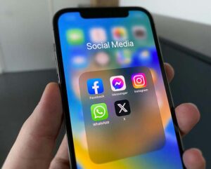 A hand holding an iPhone displaying social media icons.